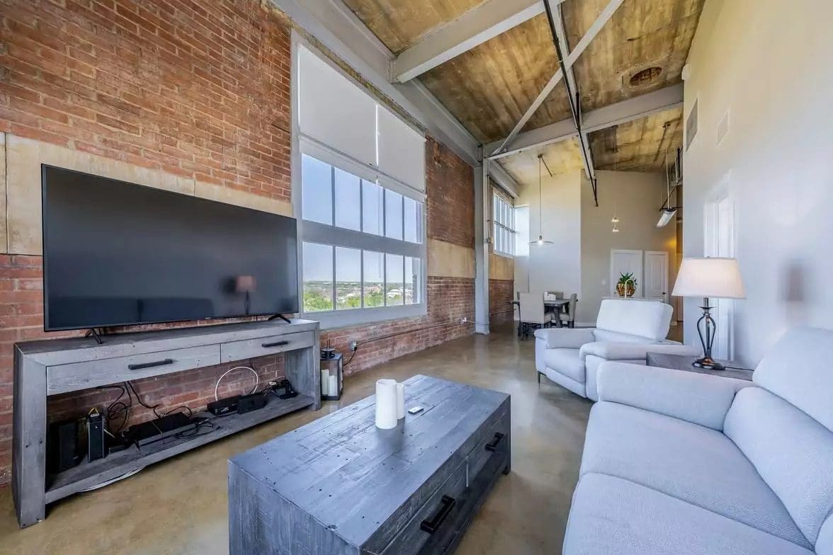 Industrial living room with brick wall and large tv, wooden table, and white couch.